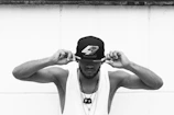 man in white tank top wearing black and white fitted cap