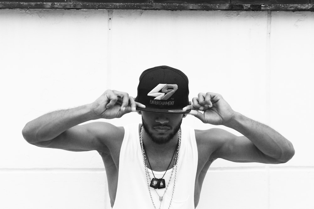 man in white tank top wearing black and white fitted cap