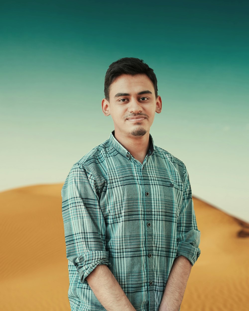 man in blue and white plaid button up shirt sitting on yellow sand during daytime