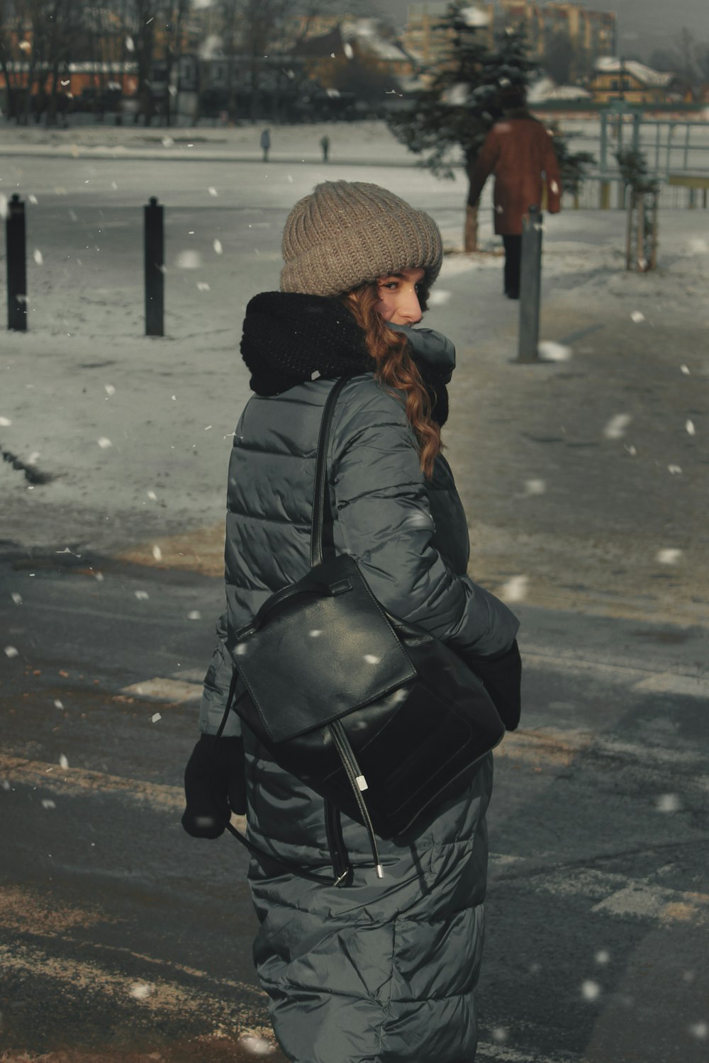 黒い革のジャケットと茶色のニット帽をかぶった女性が昼間、道路に立つ
