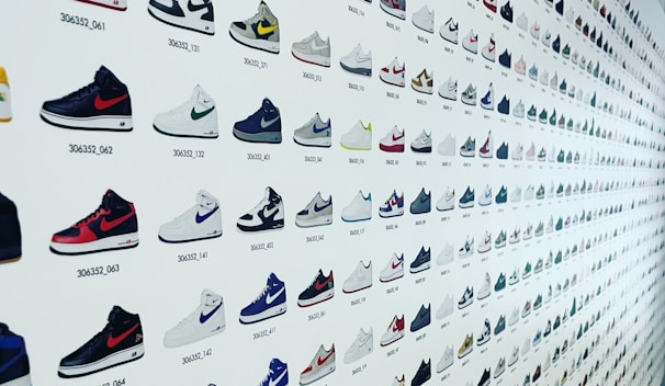 A wall featuring a vast array of Nike sneakers, presented in a grid format. Each sneaker is accompanied by a unique number code. The designs vary in color and style, ranging from high-top to low-top, and incorporating various color patterns and combinations.