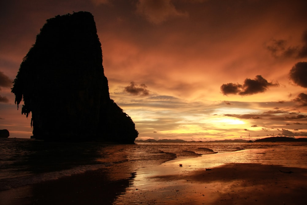 silhouette of rock formation on sea during sunset