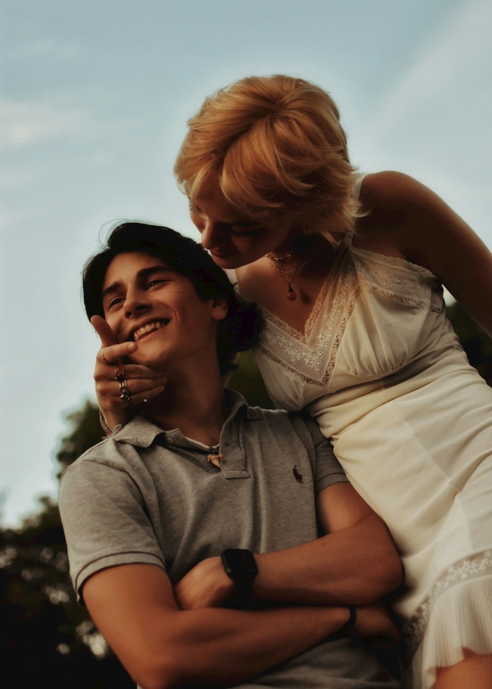 man in gray polo shirt kissing woman in white sleeveless dress