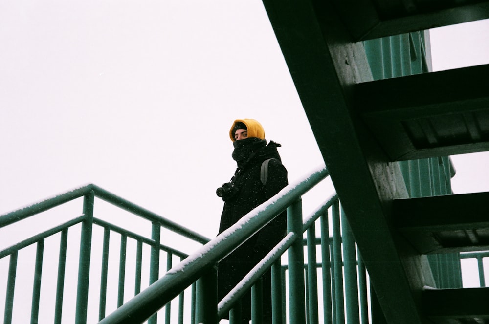 man in black jacket and yellow cap standing on the bridge