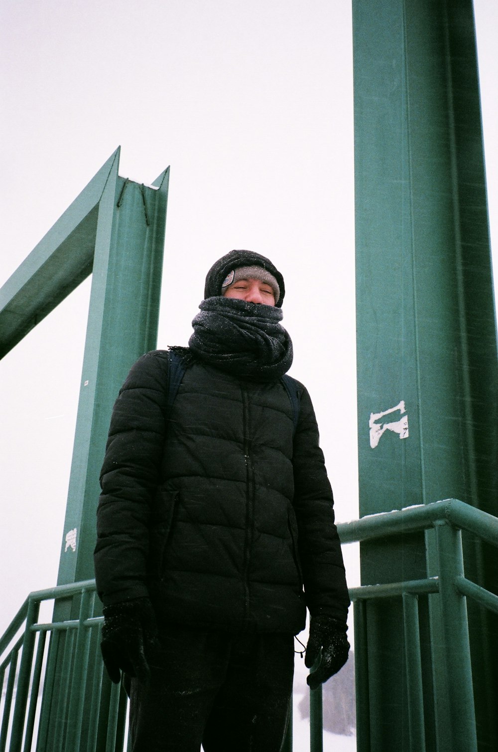 man in black jacket standing near green metal post