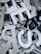 A jumble of variously sized and shaped metallic and plastic letters, predominantly in shades of silver, white, and black. Some letters are stacked on top of others, creating a chaotic and dense arrangement. A metallic screw is visible amidst the letters, adding to the industrial feel.