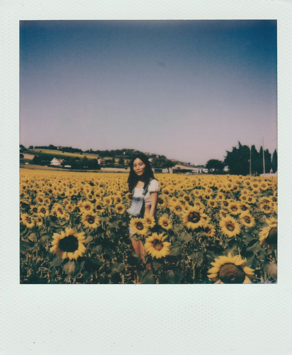 Mujer con camiseta sin mangas negra y pantalones cortos blancos de pie en el campo de girasoles durante el día