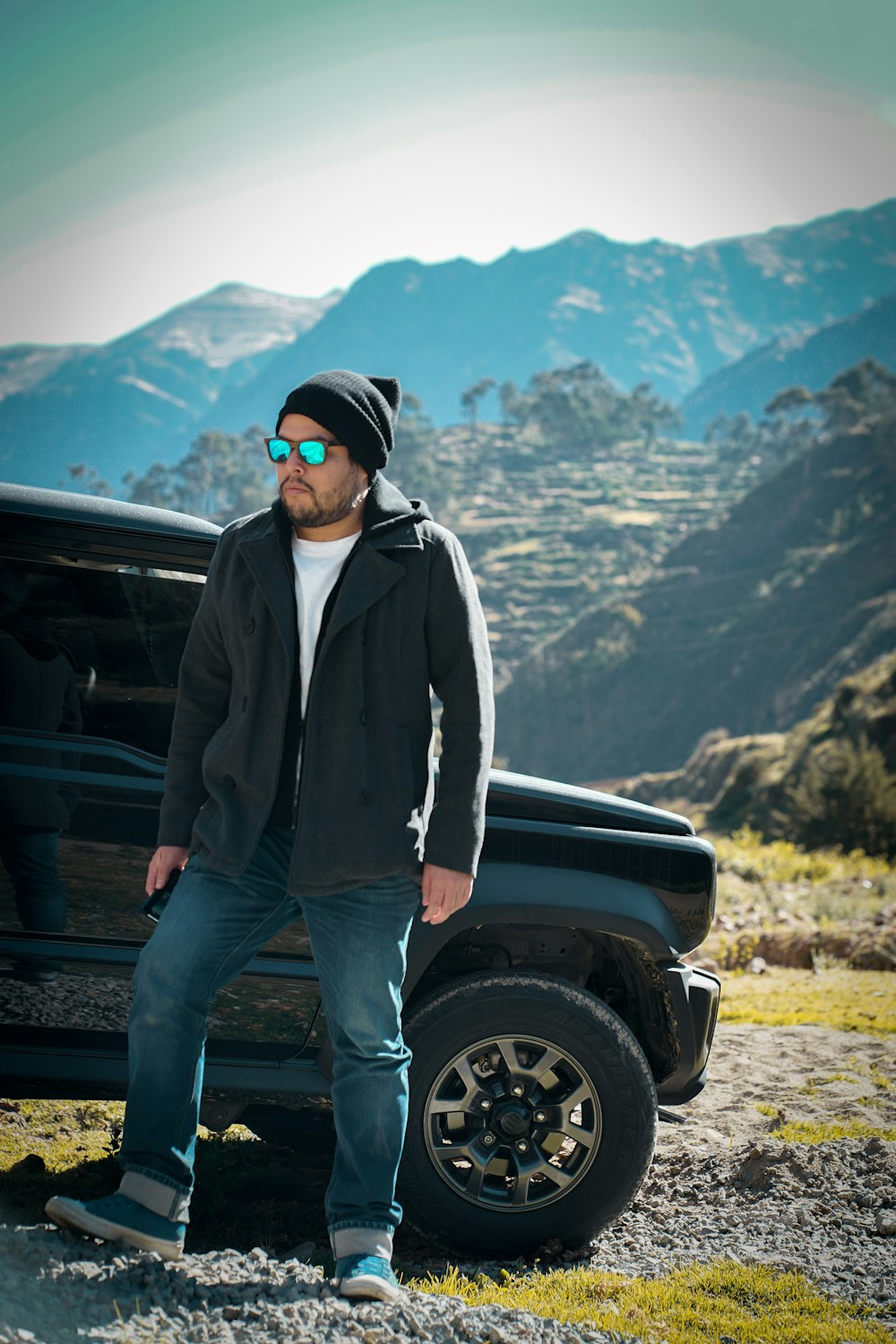 man in black jacket and blue denim jeans standing beside black car