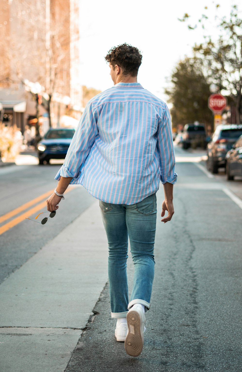 man in blue dress shirt and blue denim jeans walking on street during daytime