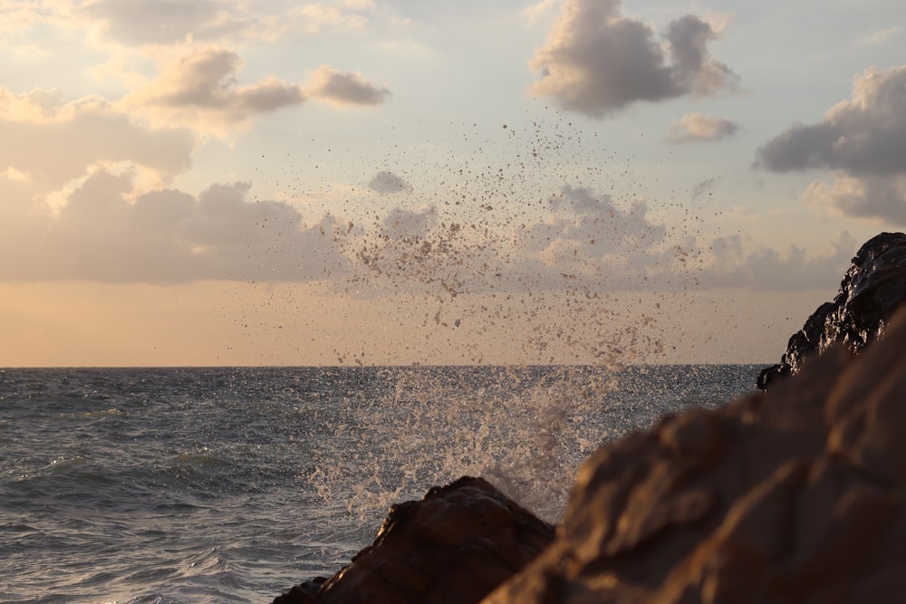 ocean waves crashing on rock formation under white clouds during daytime