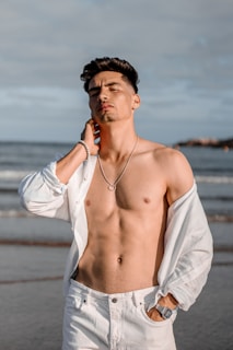 A serene beach scene with a model wearing a crisp white linen shirt from Awlak Nee, sunlight casting soft shadows.