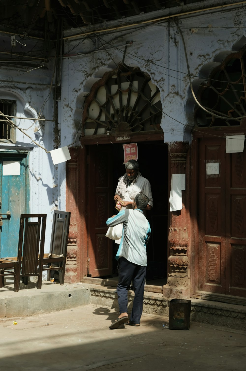 man in white dress shirt and blue denim jeans standing near brown wooden door during daytime