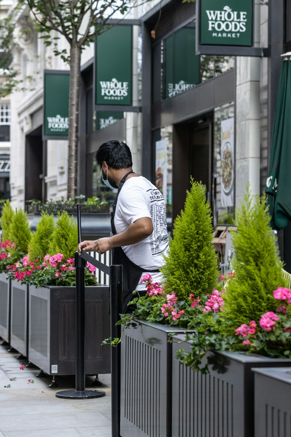 man in white t-shirt standing near flowers and building during daytime