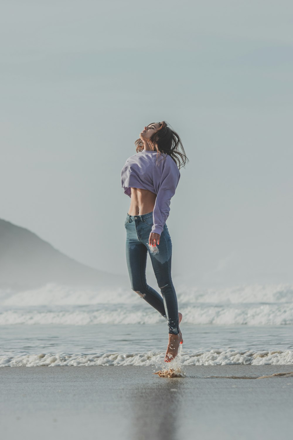 woman in white shirt and blue denim jeans standing on beach during daytime