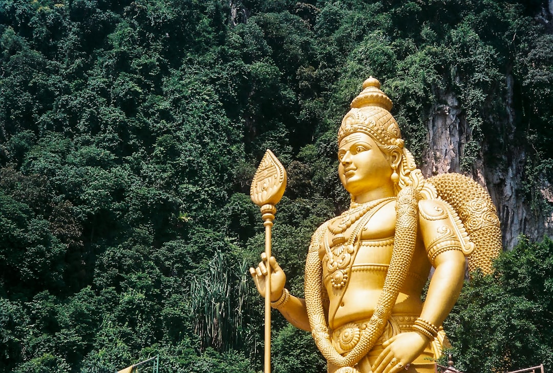 gold hindu deity statue near green trees during daytime
