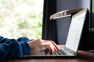 A friendly person typing on a laptop with rentiva interface on screen, sunlight filtering through window.
