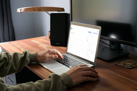 A person happily working on a laptop from a cozy home office with navy blue and green accents.