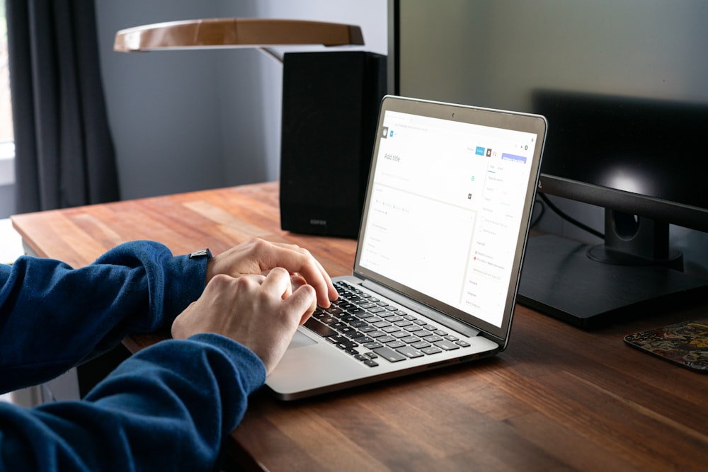 person using macbook pro on brown wooden table