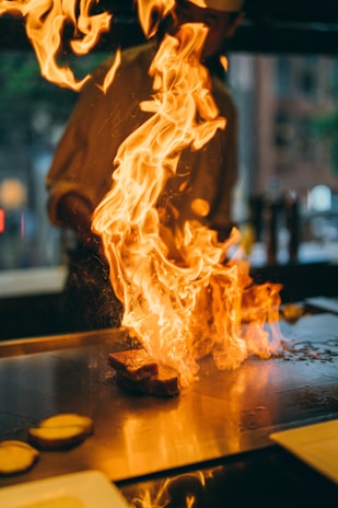 A hibachi chef mid-performance, flames rising as they cook on a portable grill at a backyard party.