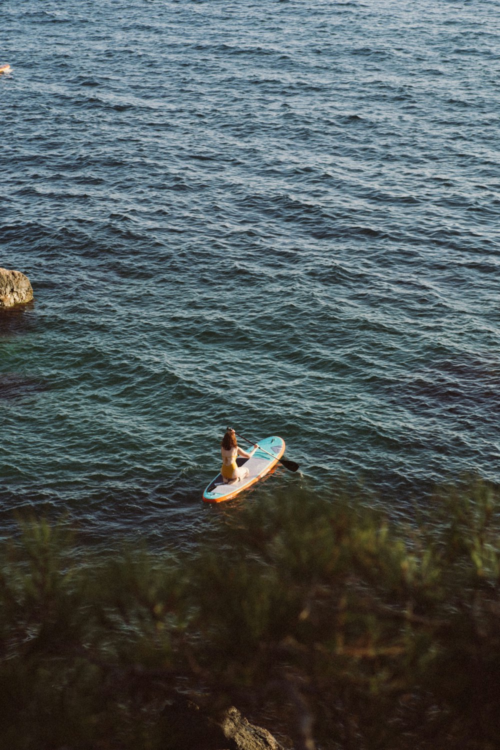 woman in yellow and white dress lying on brown surfboard on body of water during daytime