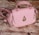 A pink handbag with a quilted pattern, gold hardware, and a distinctive raindrop-shaped embellishment on the front. It rests on a textured wooden surface, giving a rustic contrast to the bag's elegant design.