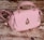 A pink handbag with a quilted pattern, gold hardware, and a distinctive raindrop-shaped embellishment on the front. It rests on a textured wooden surface, giving a rustic contrast to the bag's elegant design.