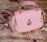 A pink handbag with a quilted pattern, gold hardware, and a distinctive raindrop-shaped embellishment on the front. It rests on a textured wooden surface, giving a rustic contrast to the bag's elegant design.