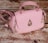 A pink handbag with a quilted pattern, gold hardware, and a distinctive raindrop-shaped embellishment on the front. It rests on a textured wooden surface, giving a rustic contrast to the bag's elegant design.