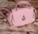 A pink handbag with a quilted pattern, gold hardware, and a distinctive raindrop-shaped embellishment on the front. It rests on a textured wooden surface, giving a rustic contrast to the bag's elegant design.