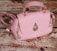 A pink handbag with a quilted pattern, gold hardware, and a distinctive raindrop-shaped embellishment on the front. It rests on a textured wooden surface, giving a rustic contrast to the bag's elegant design.