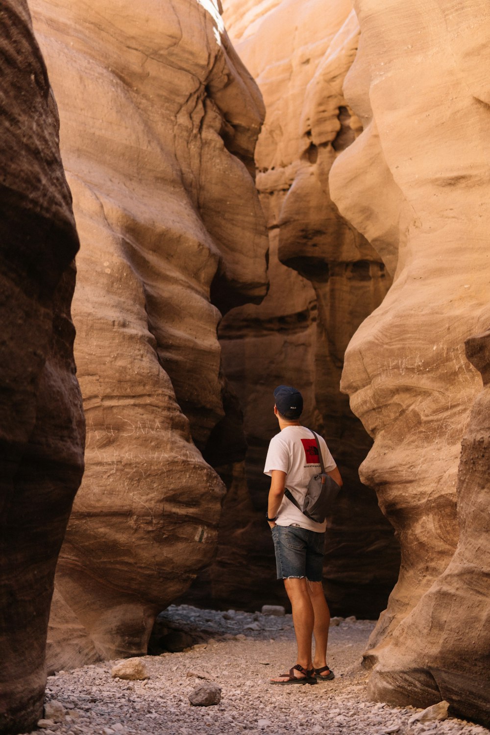 man in white t-shirt and blue denim shorts standing on brown rock formation during daytime