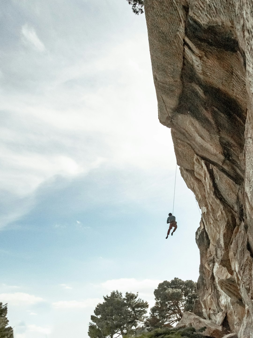 man in black jacket and black pants hanging on brown rock during daytime