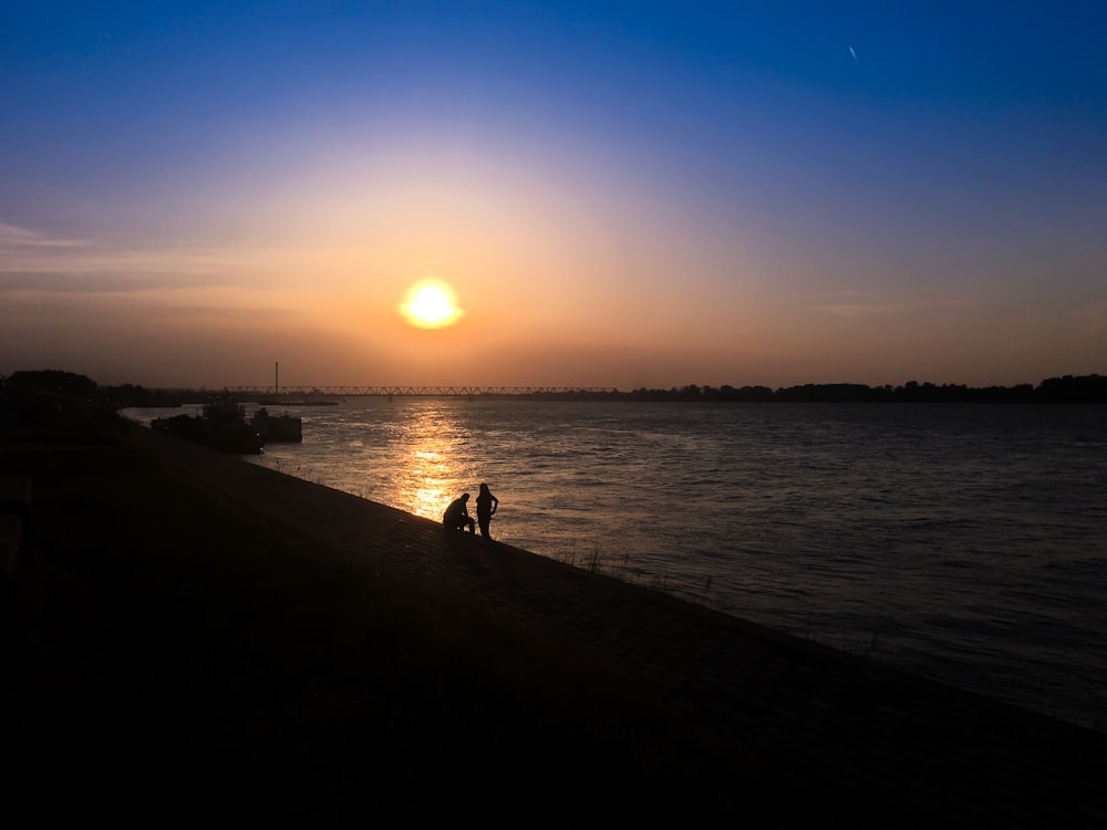 silhouette of 2 people walking on beach during sunset