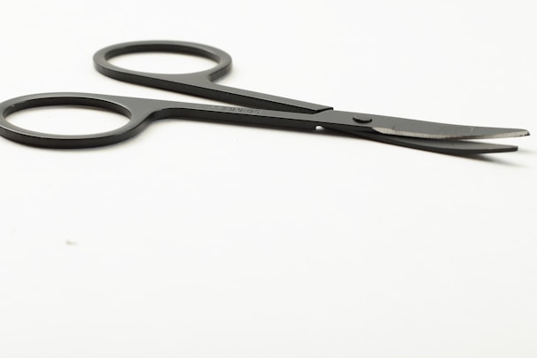 Close-up of stainless steel surgical scissors resting on a clean white surface with a soft green background.