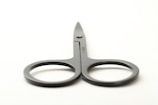 A pair of gray metal scissors with round handles and a slightly pointed blade placed on a plain light background.