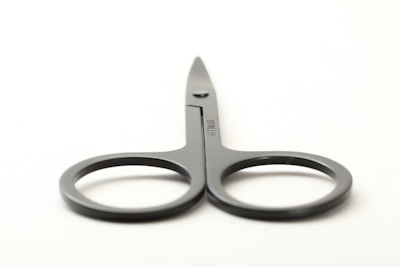 A pair of gray metal scissors with round handles and a slightly pointed blade placed on a plain light background.