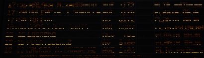 A dark background featuring rows of illuminated orange and yellow text and numbers, resembling an information board or a flight schedule display.