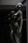 A sleek and reflective humanoid robot stands against a dark background. The robot's surface is glossy and metallic, giving it a futuristic and high-tech appearance. The structure of the robot is humanoid with defined limbs and a head, and it appears to be contemplating or observing something. The dark and reflective environment around the robot emphasizes its metallic features.