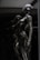 A sleek and reflective humanoid robot stands against a dark background. The robot's surface is glossy and metallic, giving it a futuristic and high-tech appearance. The structure of the robot is humanoid with defined limbs and a head, and it appears to be contemplating or observing something. The dark and reflective environment around the robot emphasizes its metallic features.