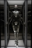 A humanoid robot with a futuristic design stands in an illuminated display case. The robot has a sleek, metallic body with articulated joints and a smooth, reflective surface. Its head is shaped with minimalistic features, including a visor-like element covering where eyes would be. The robot is positioned upright with arms slightly extended to the sides.