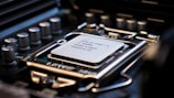 A close-up view of a computer processor installed on a motherboard, showing intricate details of the CPU socket and surrounding electronic components. The processor is labeled with technical specifications, emphasizing the precision and complexity of computer hardware design.