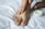 A person's hand is applying cream to their foot on a white bed. The scene captures a moment of personal care and relaxation.