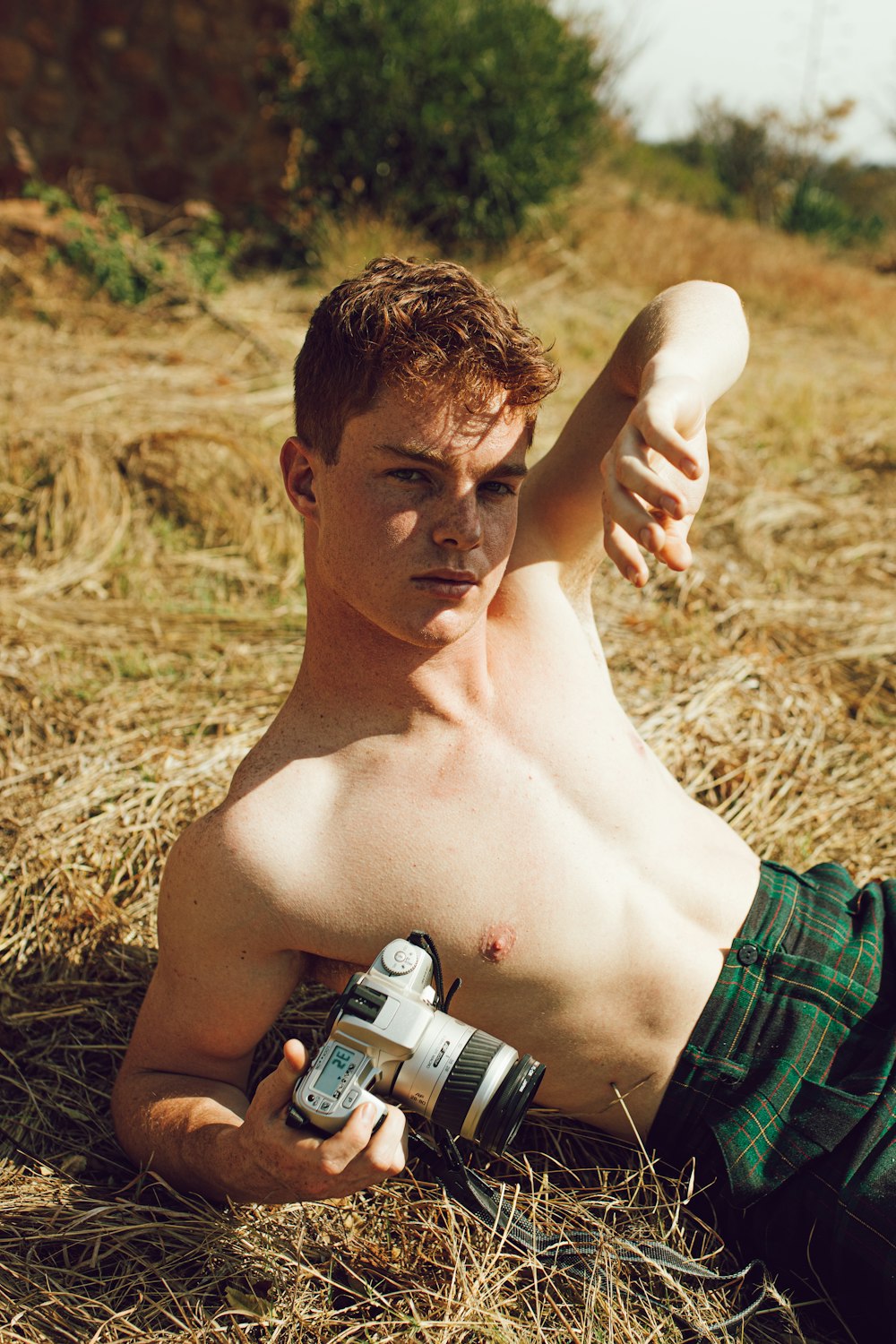 man lying on brown grass field holding gray camera