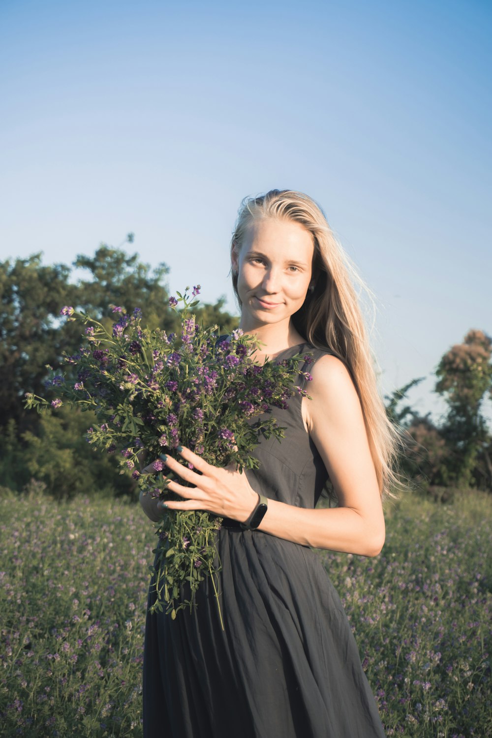 woman in black spaghetti strap dress holding purple flowers