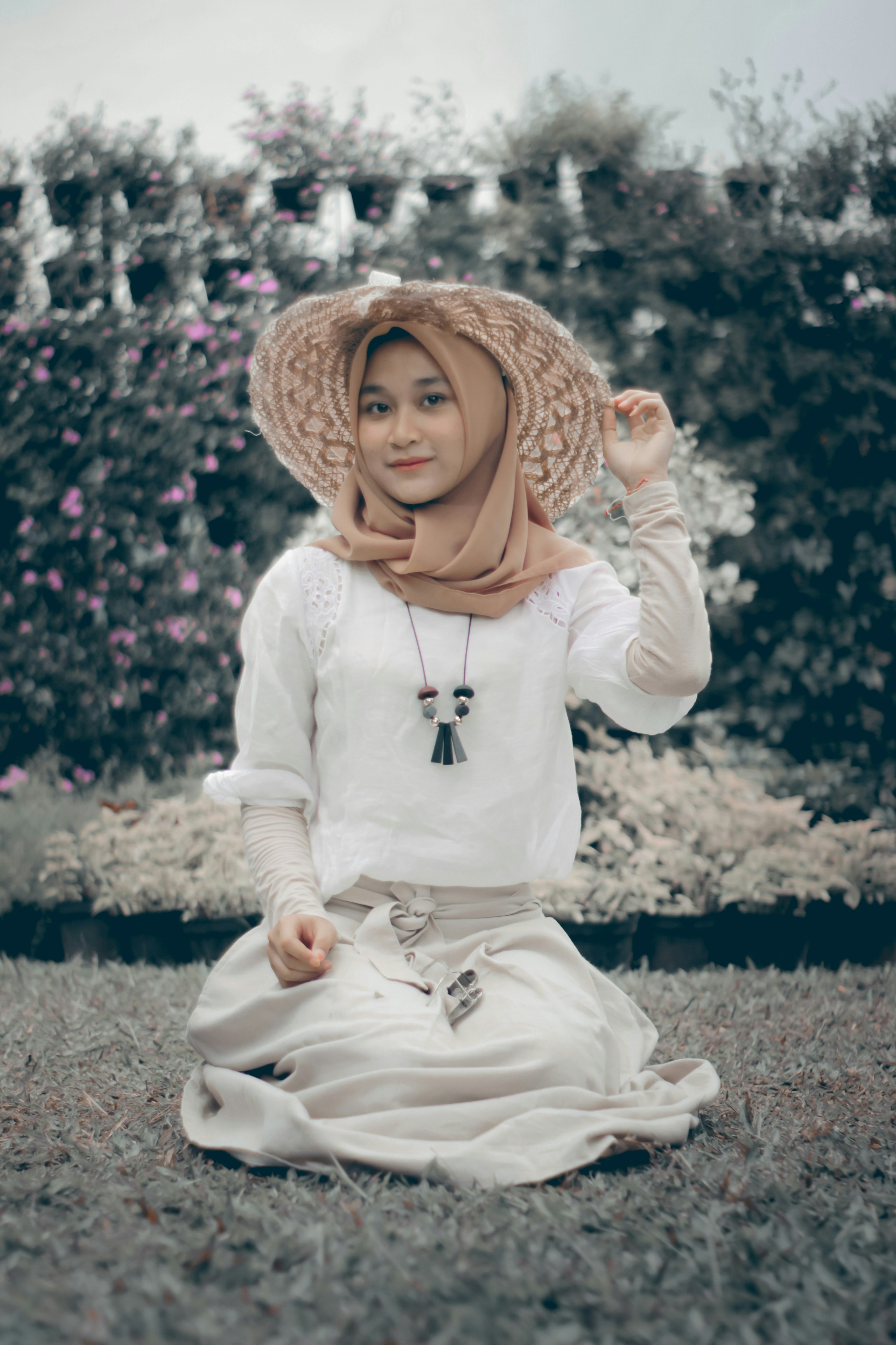 Wanita muda berjilbab dan topi duduk di atas rumput
