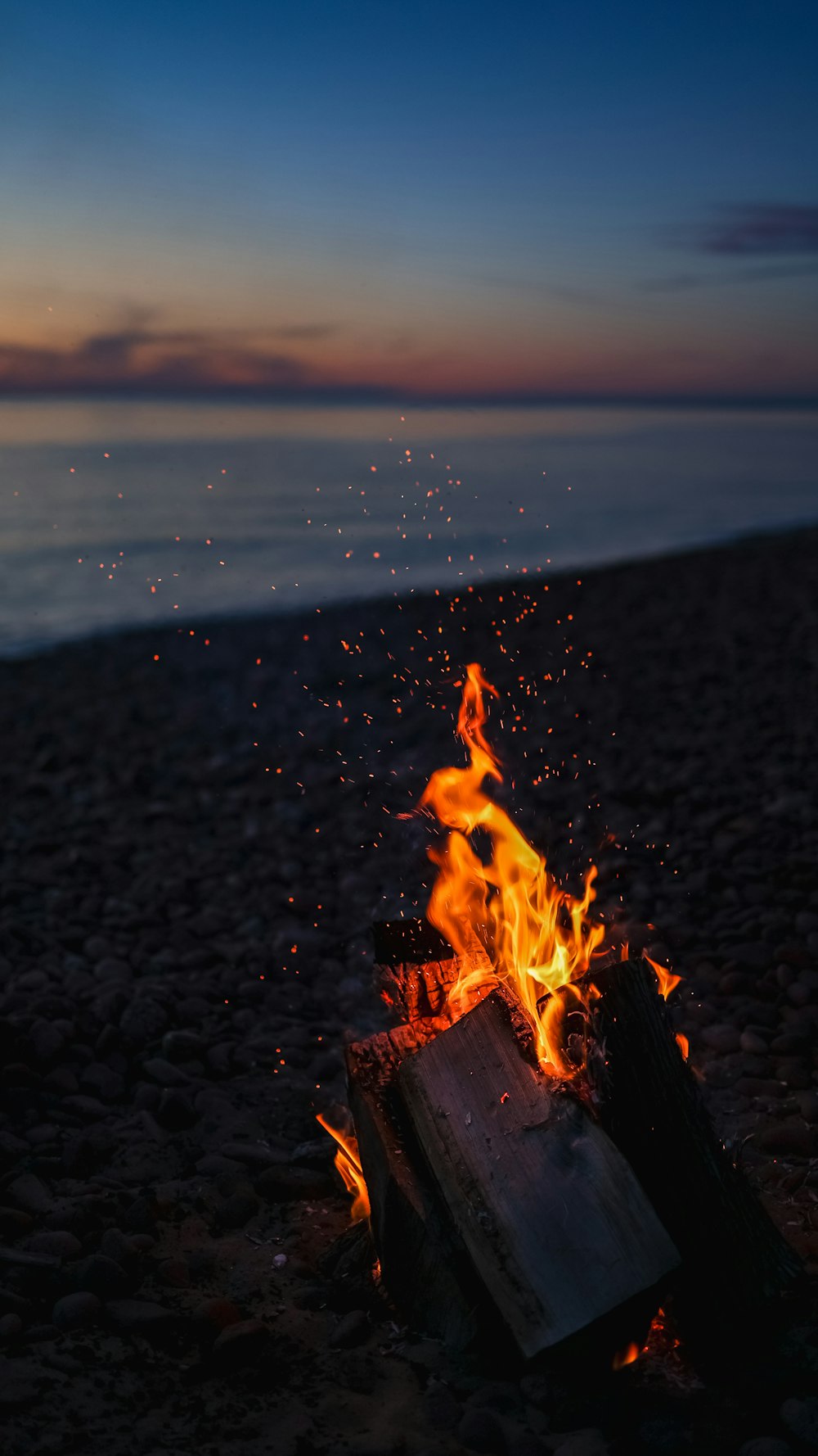 Feuer auf braunem Sand in der Nähe von Gewässern während des Sonnenuntergangs