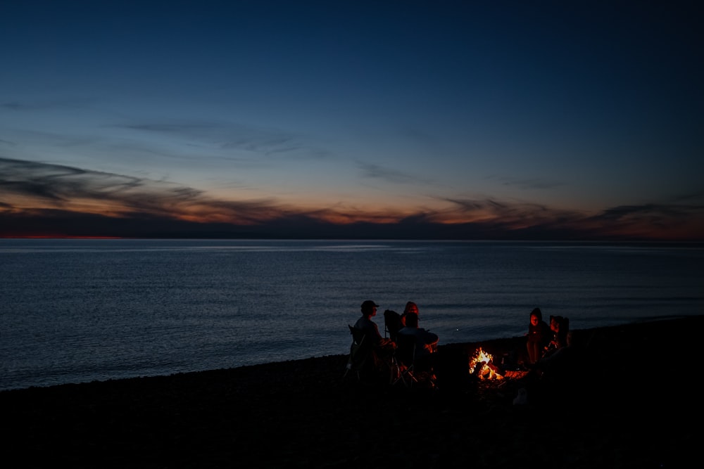 日没時に水辺の岩の上に座っている人々のシルエット