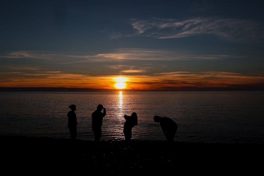 silhouette of people standing on seashore during sunset