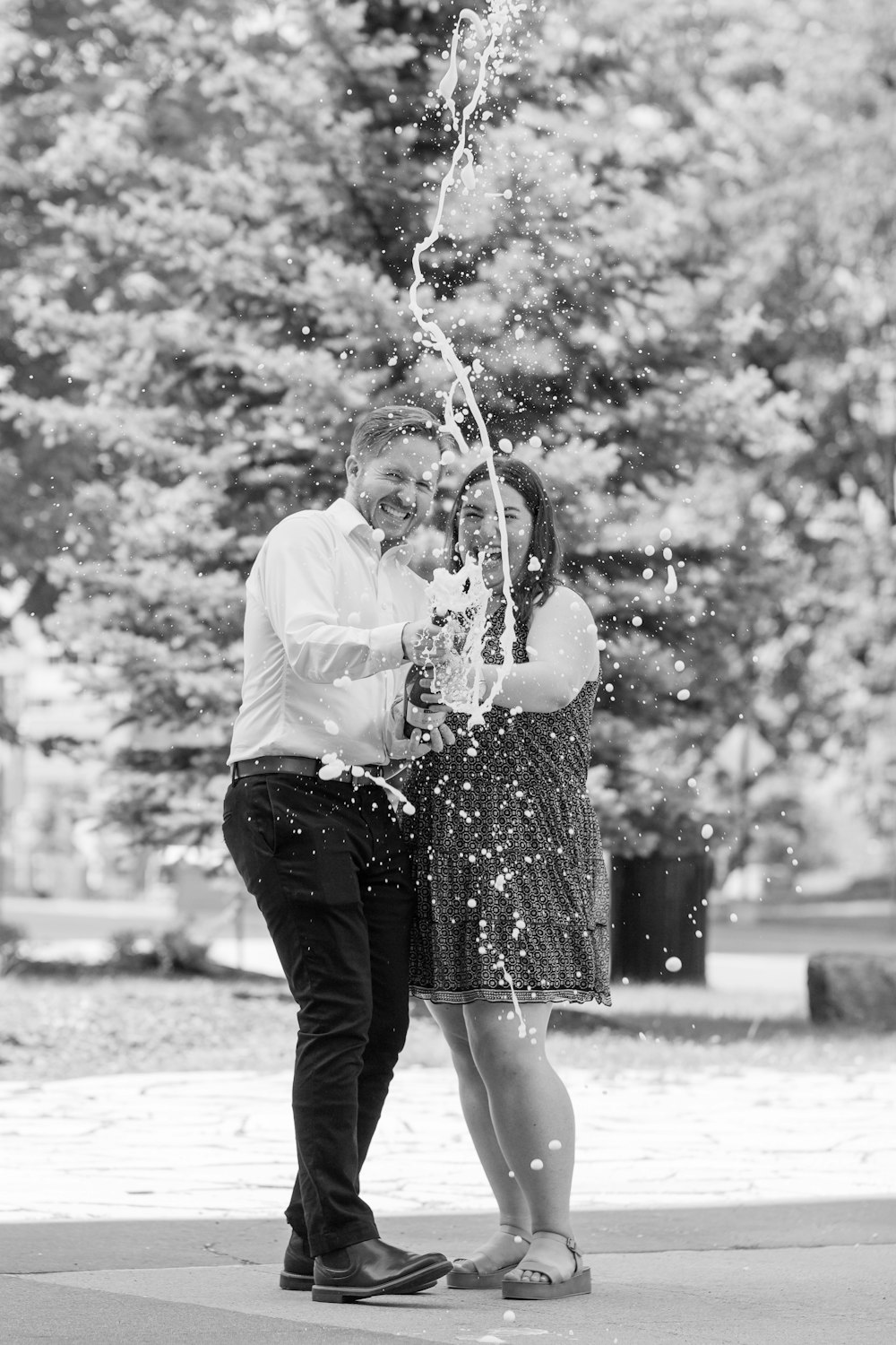 grayscale photo of woman in white dress shirt and black skirt holding string lights