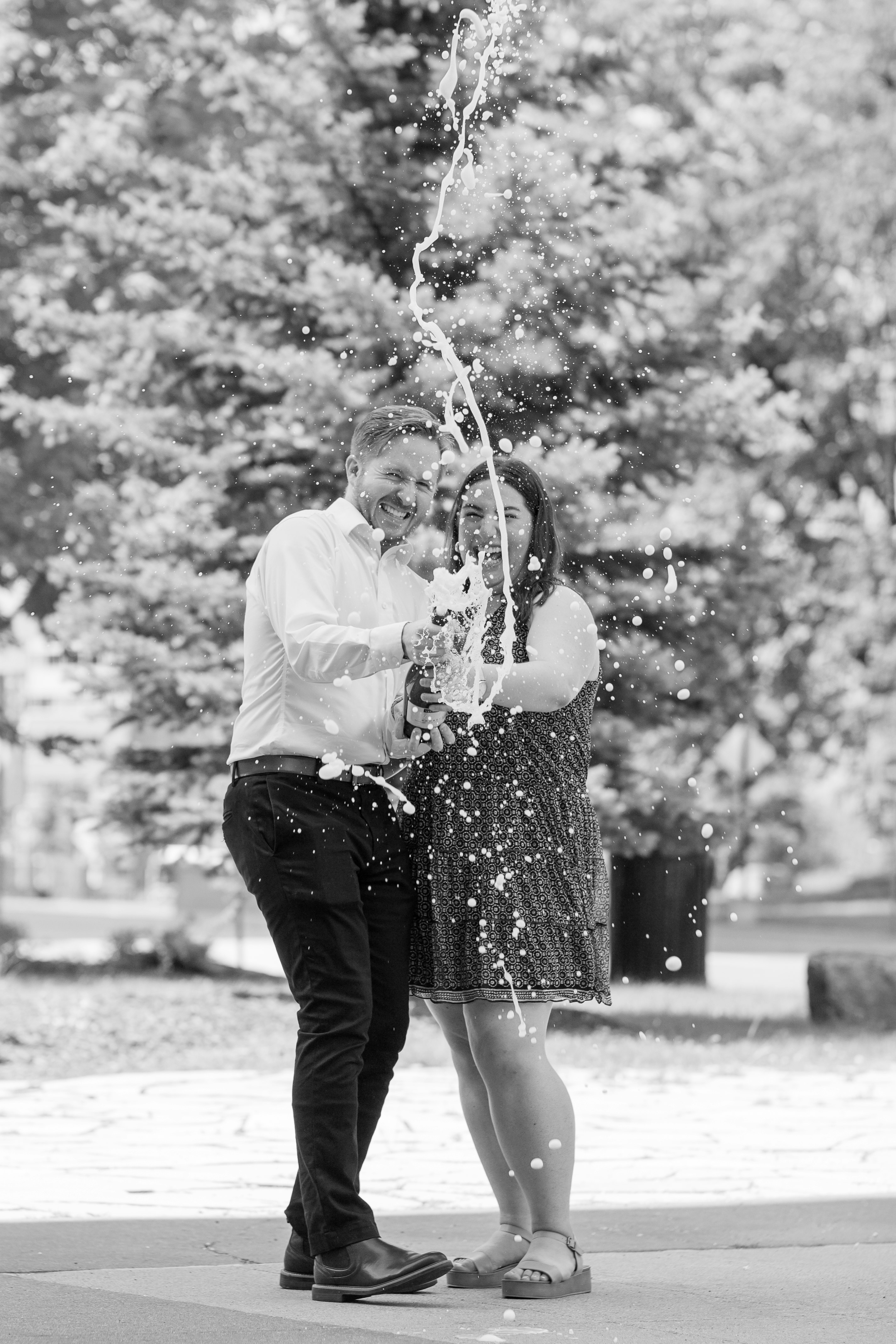 grayscale photo of woman in white dress shirt and black skirt holding string lights